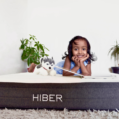 Smiling child lying on a HIBER mattress with a stuffed animal, showcasing comfort and kid-friendly design.