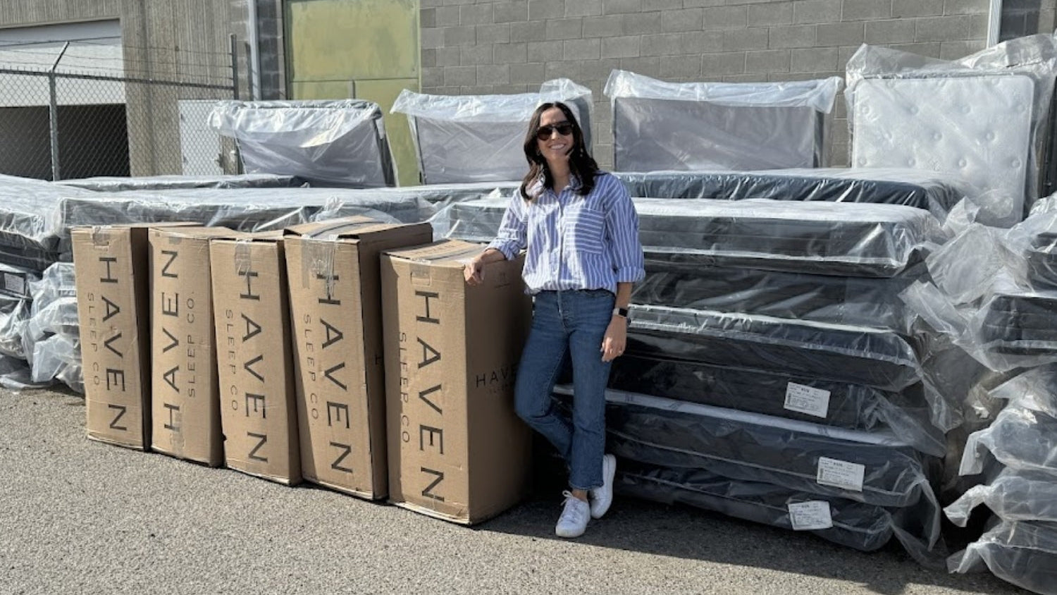 Woman standing next to Haven branded boxes and mattresses outside a building on charity donation day