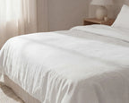 White comforter on a bed in a bedroom setting with a lamp and nightstand.