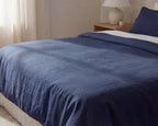 Navy blue comforter on a bed in a bedroom setting with a lamp and nightstand.