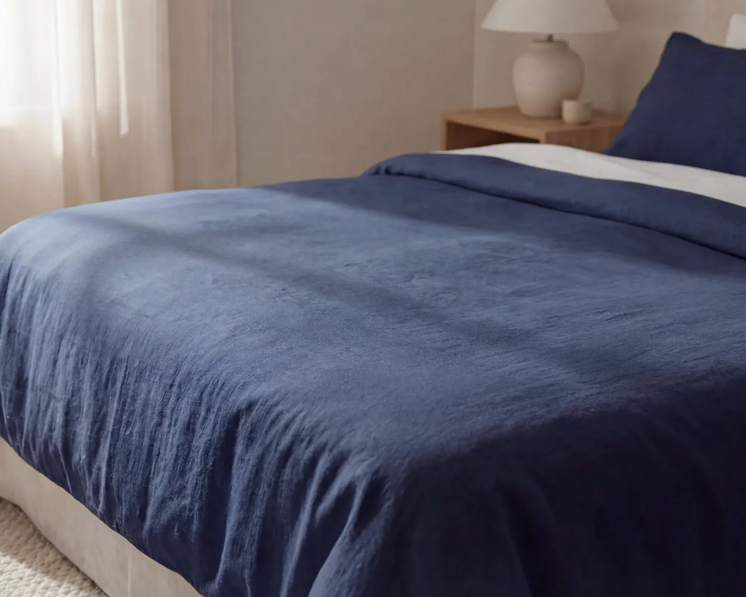 Navy blue comforter on a bed in a bedroom setting with a lamp and nightstand.