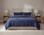 Blue bedding set on a bed in a bedroom with two nightstands and lamps.