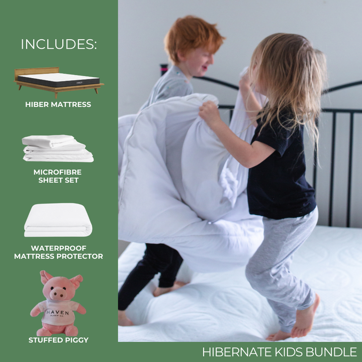 Two children having fun on a bed while playing with a white blanket, part of the HIBERNate Kids Bundle. The bundle includes a HIBER NaturFoam Mattress, a waterproof mattress protector, a microfiber sheet set, and a Haven Limited Edition Ester the WonderPig stuffed toy.