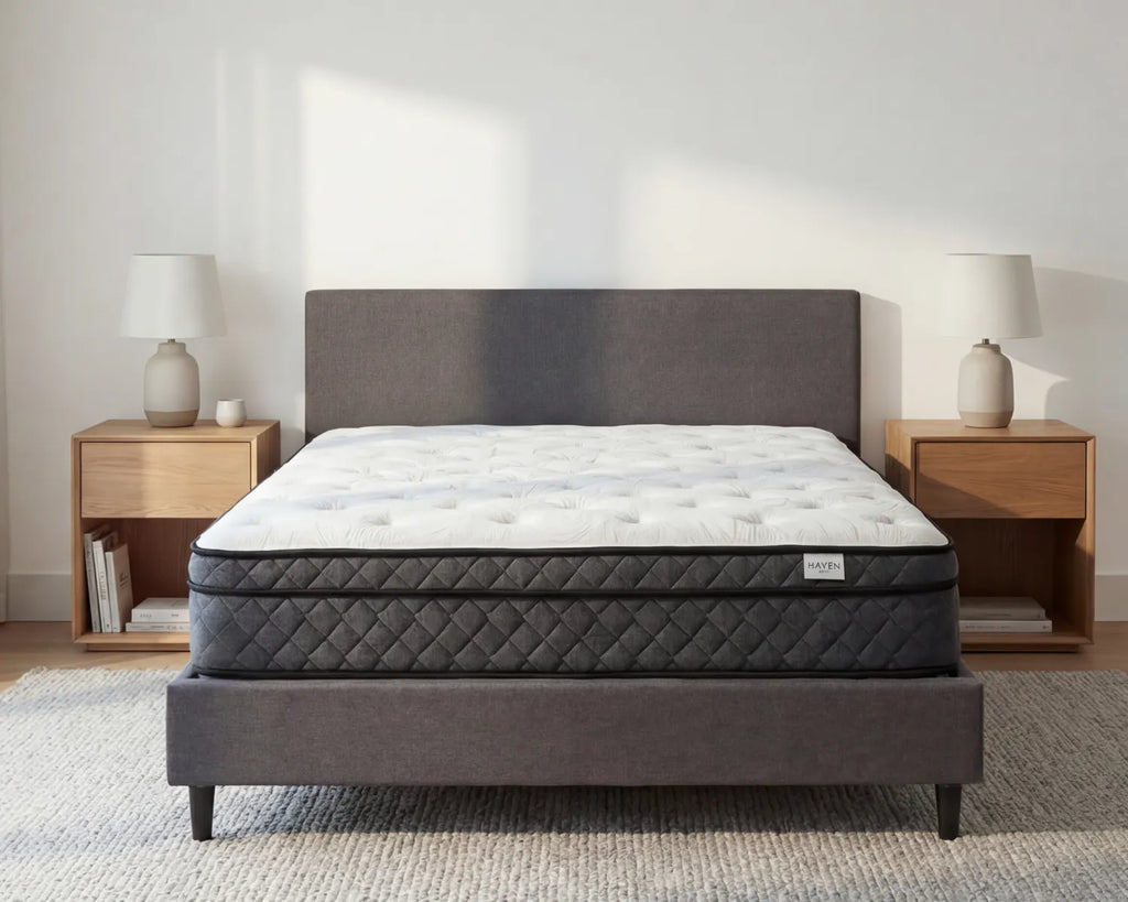 Gray mattress on a bed frame in a bedroom setting with nightstands and lamps.