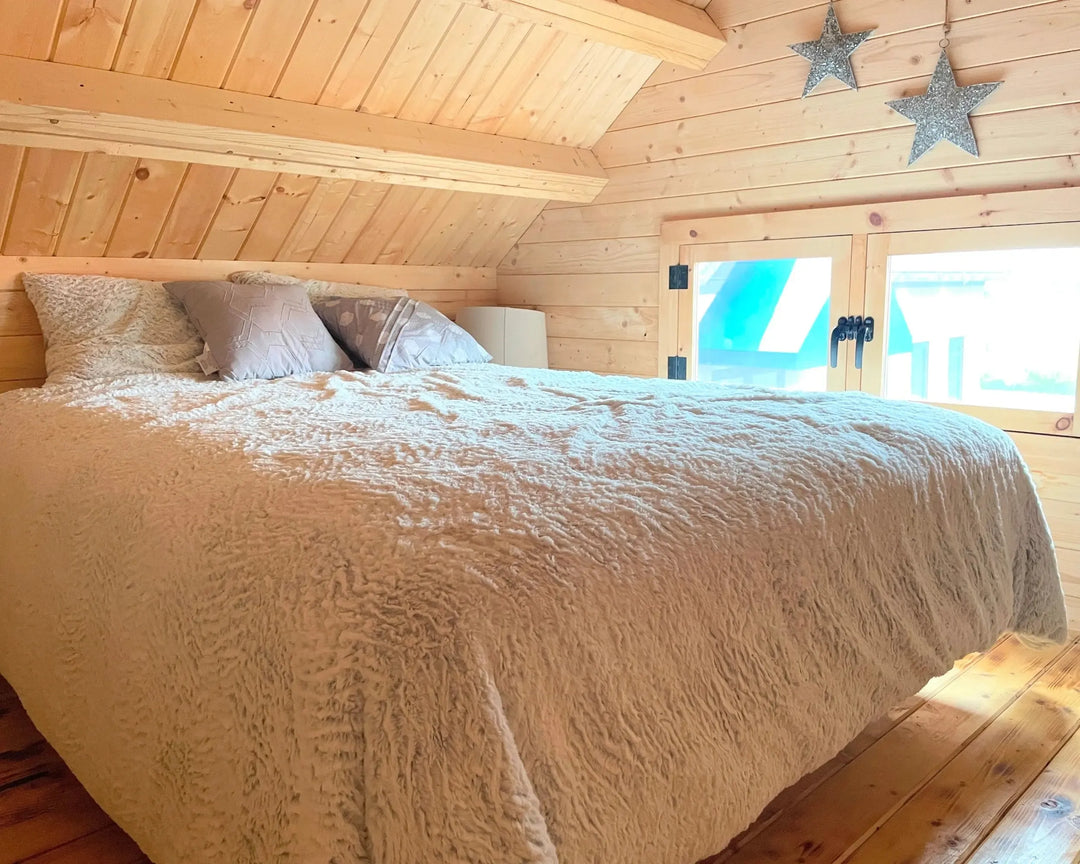 Bedroom with wooden walls and ceiling, featuring a bed with beige bedding.