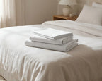 Stack of white folded bed sheets on a bed in a bedroom setting