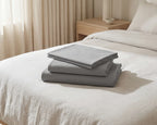 Gray bed sheets stacked on a bed with a neutral background
