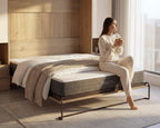 Woman sitting on a bed holding a mug in a modern bedroom with 'Hiber' mattress.