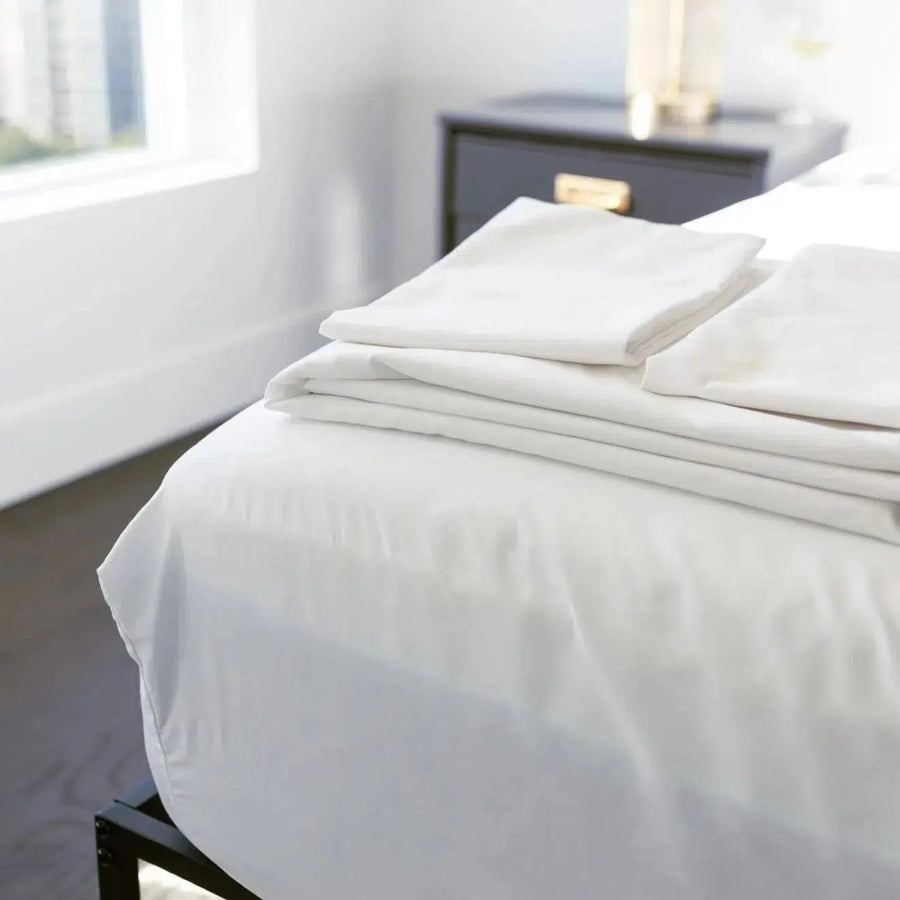 Crisp and Cool Percale sheet set neatly folded on a bed in a bright, modern bedroom