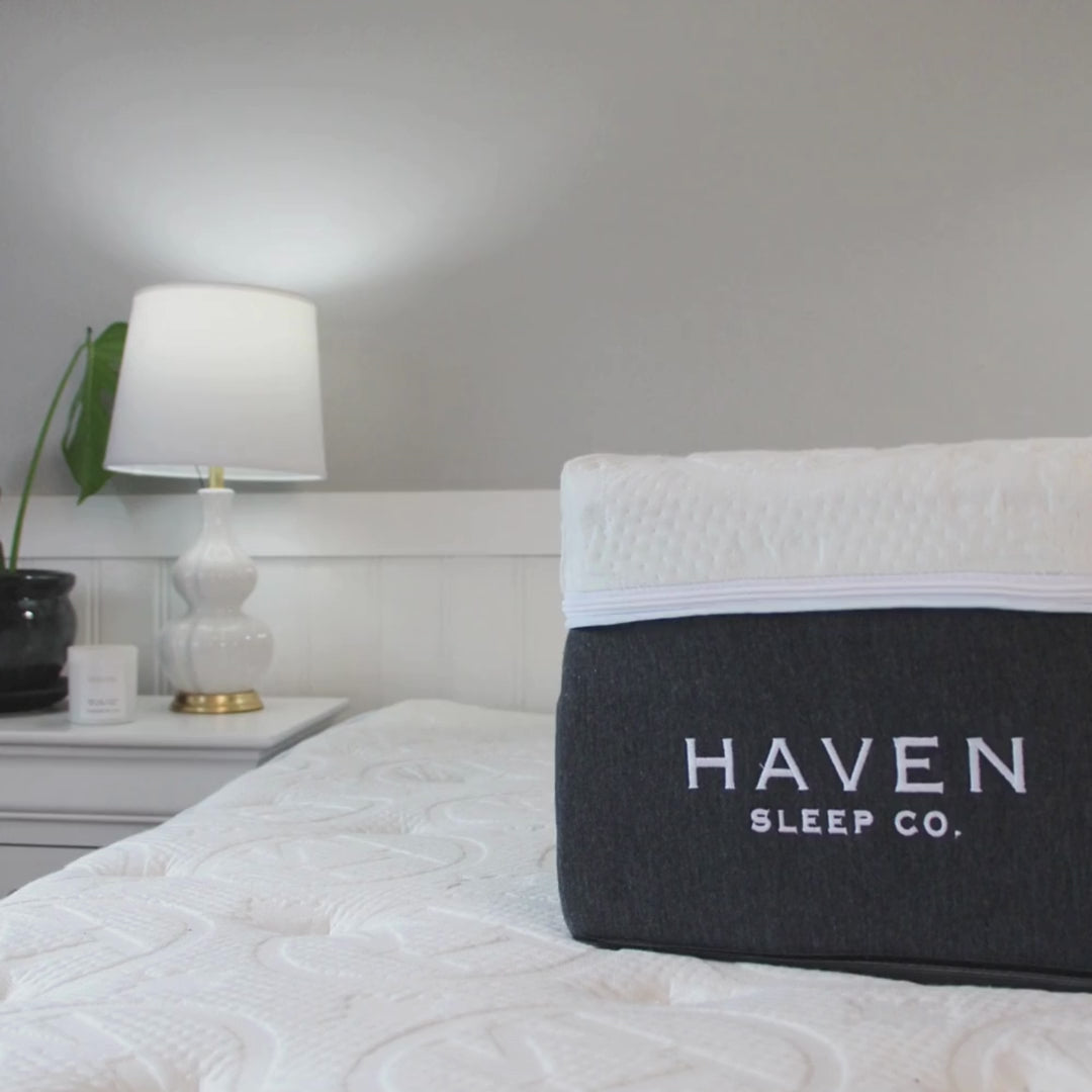Cross-section view of the Haven LUX Rejuvenate Mattress showcasing its multiple cooling layers, displayed in a serene bedroom setting with a bedside lamp.