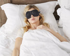 Woman in white sleeping with a pair of Bedface Blacjout 40 blinks sleep mask in black on memory foam pillow and Haven mattress in Starlight white sheet set with a white duvet cover pulled up to cover her