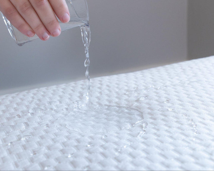 Close up of a hand pouring a glass of water onto a Bedface Artic Cooling Mattress protector showing the protector is waterproof