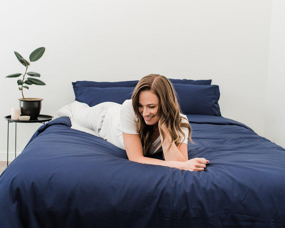 Woman in white laying across Haven Mattress with Nighttime Navy Blue bedding 