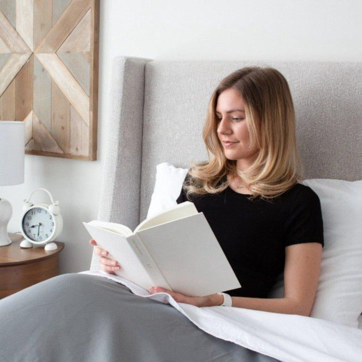 blonde women sitting up reading a book in her bedface sheets set