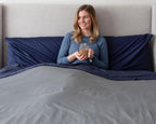 Woman sitting up in bed smiling in Bedface premium sheet set and duvet cover - storm grey and night time navy