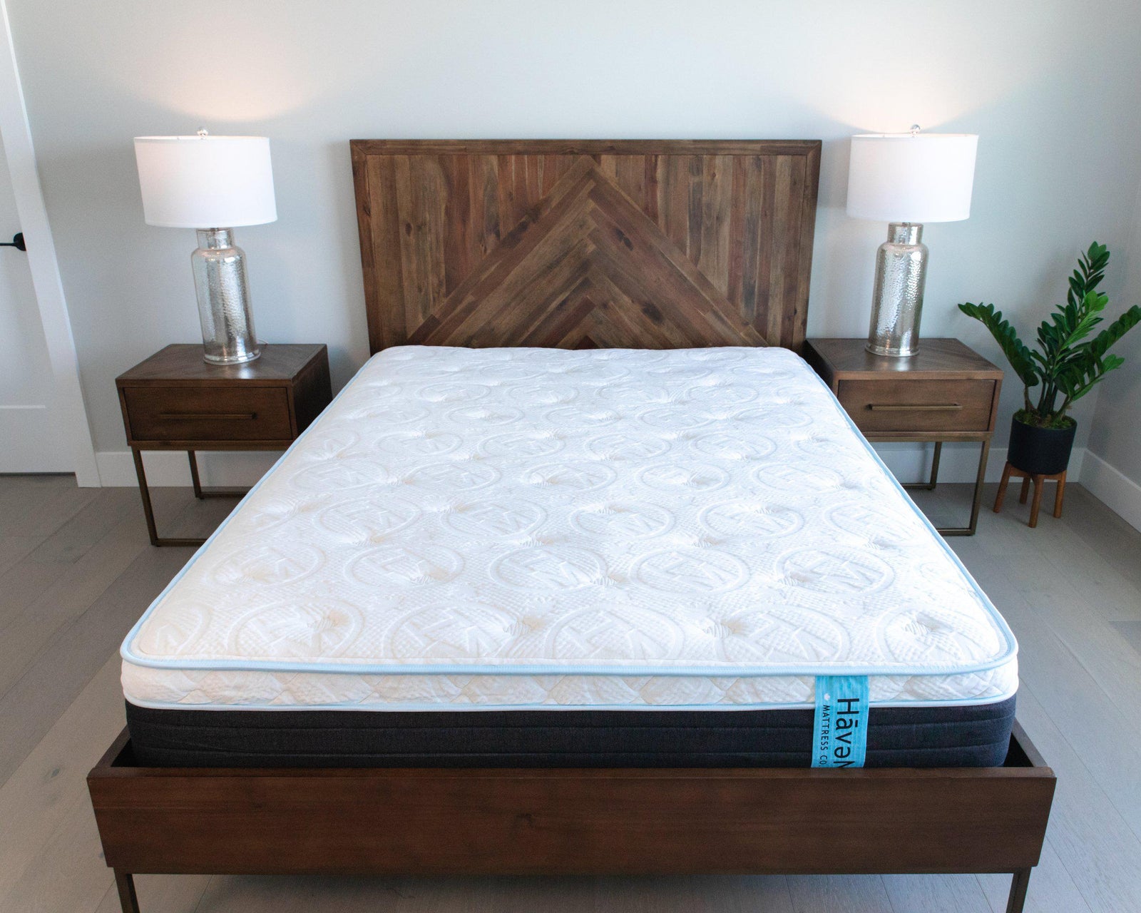 Showcase of 12" Hybrid Eurotop Haven Mattress with embossed Haven logo on top of wooden bedframe and headboard with wooden side tables and lamps