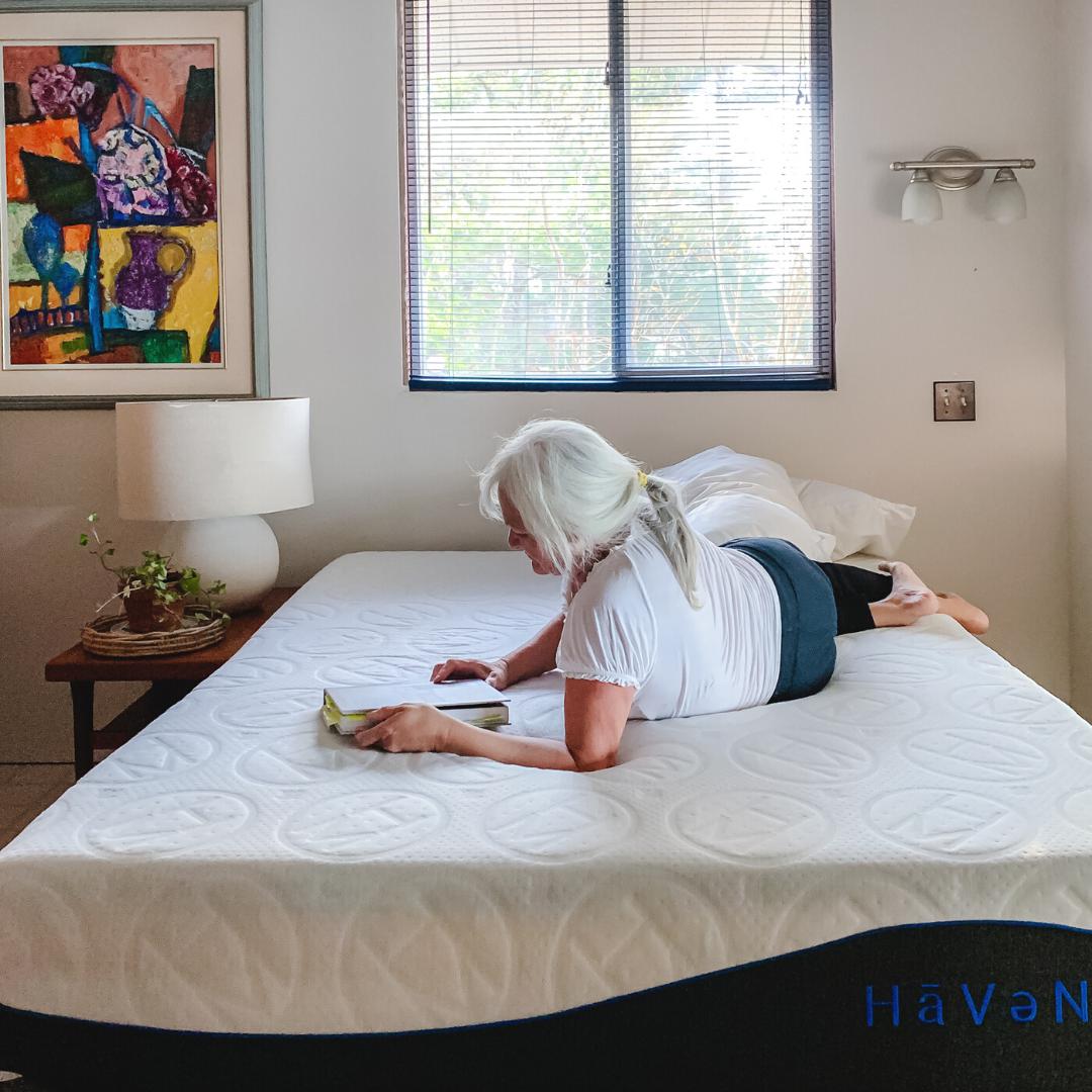 Older woman wearing white Tshirt and yoga pants laying across a 10" Essential Haven Mattress with a hardcover book